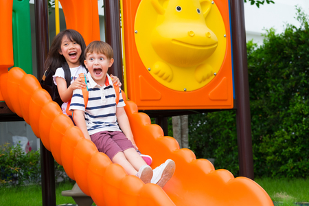 Two kids friends having fun to play together on children's slide at school playground,back to school activity.の写真素材