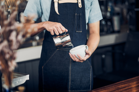 Man barista pour milk into hot coffee cup at counter bar in front of machine in cafe restaurant,Food business owner concept.の写真素材