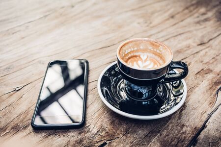 Close up hot black coffee cup and mobile on wood table near window with sunlight at cafe restaurant.Leisure lifestyle.food and drinkの写真素材