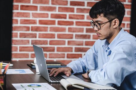 Asian businessman looking at work on laptop at office desk with serious emotion