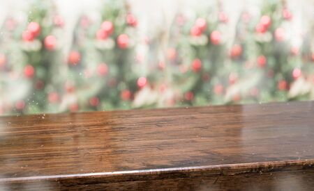 wooden table top with abstract blur christmas tree red decor ball and snow fall background with...