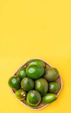organic avocados whole fruit in basket on yellow table background vertical top view.Healthy super...