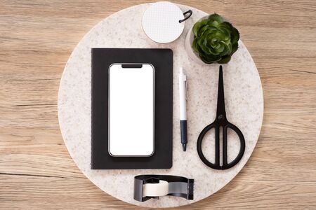 mobile mock up on office desk table top view with stationery,notebook,plant on wooden table background.smart phone screen for display of design.business object flat lay.clipping path device templateの写真素材