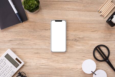 mobile mock up on office desk table top view with stationery,notebook,plant on wooden table background.smart phone screen for display of design.business object flat lay.clipping path device templateの写真素材