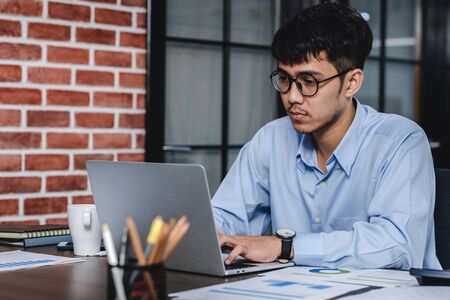 asian businessman woking with laptop and paper work on desk  at office.digital workflow online business lifestyle conceptの写真素材