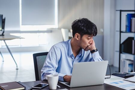 asian businessman get stress and thinking when working with laptop on desk at modern office.business fail concept.man rest hand on chin on table when stuck out of ideaの写真素材