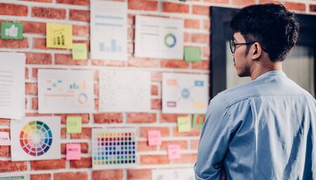 Asian man creative director designer looking at data chart and find idea on brickwall at modern office.brainstroming creative ideas concpetの写真素材