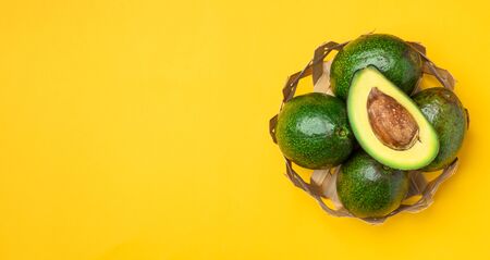 organic avocados half cut with seed and whole fruit in basket on yellow table background.Healthy super foods for diet.Fresh vegetable from farm.keto food ingredients.banner top viewの写真素材