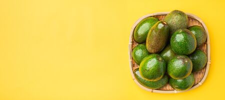 organic avocados whole fruit in basket on yellow table background vertical top view.Healthy super foods for diet.Fresh vegetable from farm.keto food ingredients.banner mock up for display contentの写真素材