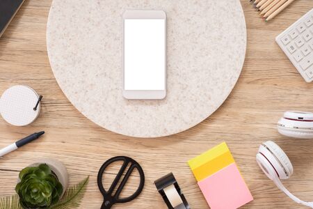 mobile mock up on office desk table top view with stationery,notebook,plant on wooden table background.smart phone screen for display of design.business object flat lay.clipping path device templateの写真素材