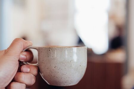 Close up hand holding a cup of hot cappuccino coffee cup with heart shape latte art blur cafe interior.food and drink concept.copy space for adding textの写真素材