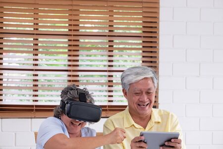Asian senior couple play virtual realtiy glasses headset and tablet watching vr video and  have fun together in living room at home.senior with technology.aging at homeの写真素材