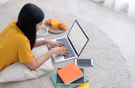 Asian female freelancer working on laptop computer at home.woman lying down on carpet at brick wall.working online lifestyle.mock up screen with clipping pathの写真素材