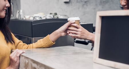 Young asian woman barista wear jean apron served to go coffee cup to customer at bar counter with smile emotion, Cafe restaurant service concept, Owner small business concept.の写真素材