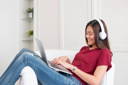 Asian woman listening music on headphone and using laptop computer with relax pose at couch in living room at home.leisure lifestyleの写真素材