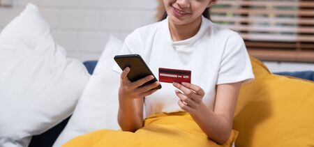 Young asian woman is holding credit card and using smartphone for online shopping.sitting on sofa.Close upの写真素材