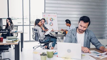 Creative designer director checking work on laptop while team is in casual meeting at background in modern office.agency lifestyle working conceptの写真素材