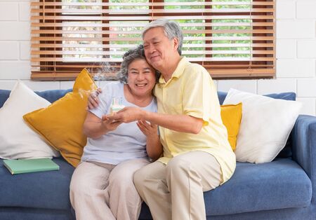 asian senior man surprise senior woman with birthday cake in living room at home.aging at home concept.の写真素材