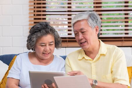 Asian senior couple use tablet searching about retirement financial document sitting on sofa at home,senior learn to use technology.aging in place conceptの写真素材