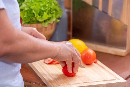Closed up senior hand slicing tomatoes on wooden cutting  board. preparing  salad,healthy concept.Retirement lifestyleの写真素材