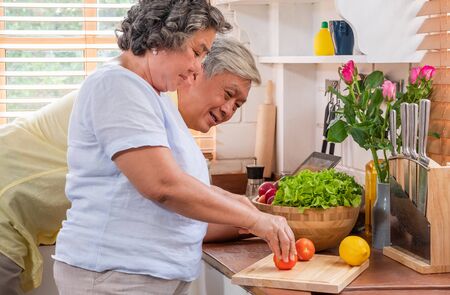 Asian senior wife slicing tomatoes on wooden cutting  board and using tablet computer to searching menu recipe.senior with technology lfiestyle.aging at homeの写真素材