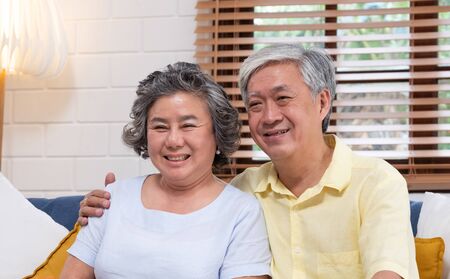Asian couple senior embracing and sitting comfortably on sofa and  watching tv in living room at home.の写真素材