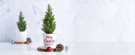 Merry christmas tree with pine cone,decor red xmas ball on wood log at white table and marble tile wall background.clean minimal simple style.holiday still life with space to adding textの写真素材