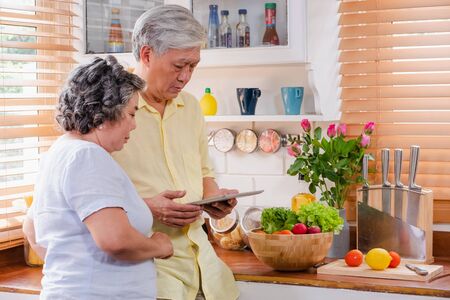Asian senior couple using tablet computer to searching menu recipe and type of vegetable in kitchen at home.senior with technology lfiestyle.aging at homeの写真素材