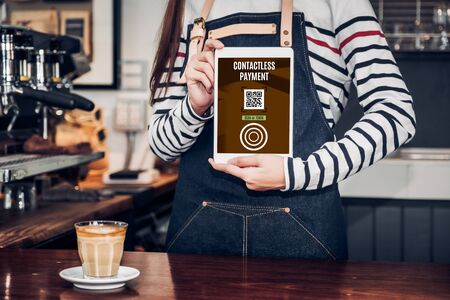 CLose up woman barista hand holding tablet with contactless payment method at counter bar in restaurant cafe.online paymentの写真素材
