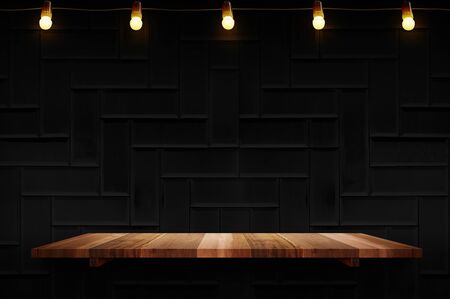 Empty brown plank wood shelf at black modern tile wall background with light bulbs string,Mockup for display or montage of product or design.の写真素材