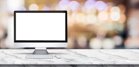 Blank screen desktop computer on marble table top with blur bar restaurant bokeh background,Mock up for display or montage of designの写真素材