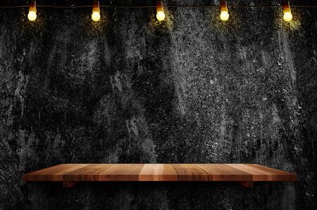 Empty brown plank wood shelf at black grung concerte wall background with light bulbs string,Mockup for display or montage of product or designの写真素材