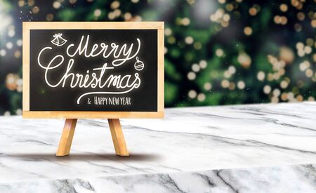 Merry Christmas on blackboard on white marble table at blur bokeh Christmas tree with string light background when snow falling,Winter holiday greeting cardの写真素材