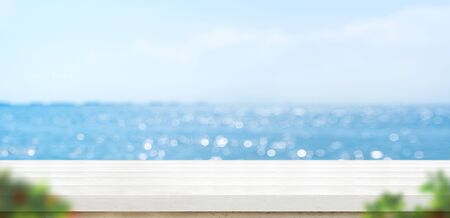 Empty white plank wood table with blur blue sky and sea bokeh background with green leaf foreground,Mock up template for display or montage of product or content use as banner in social media adsの写真素材