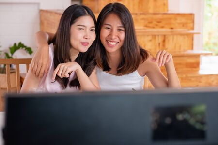 Happy asian lesbian couple watching television while eating breakfast at kitchent in cozy homeの写真素材