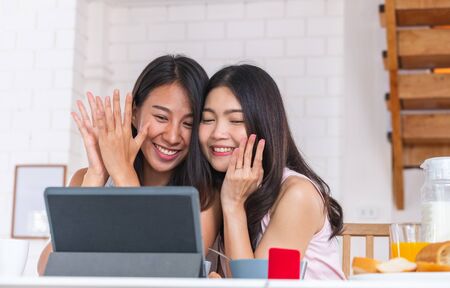 Happy asian couple lesbian getting marriage and showing ring to friend infront of tablet with video chat.LGBTQ lifestyle conceptの写真素材
