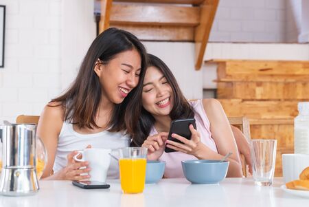 Happy asian lesbian woman couple watching morning news on mobile when have breakfast at house in morning with love and tender.LGBTQ lifestyle conceptの写真素材