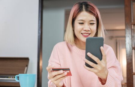 Asian woman online shopping with credit card and mobile phone at home.digital lifestyle with technologyの写真素材