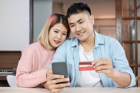 Asian couple use mobile phone shopping online with credit card together in living room at home.couple in home conceptの写真素材