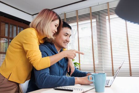 Asian couple watching video live straming on laptop at table at home.lover spending time together.take a break after workingの写真素材