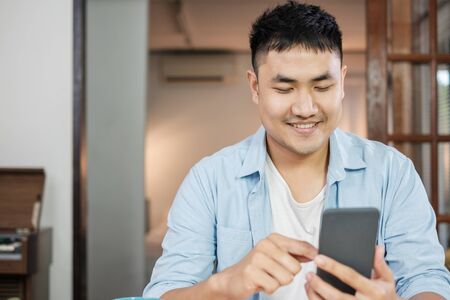 asian man using mobile rooting football tally at home in weekendの写真素材
