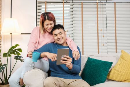 Asian couple watching video live on tablet on sofa in living room at home.lover spending time togetherの写真素材
