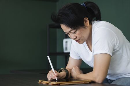 asian woman writing on tablet on table at home.work from home while coronavirus outbreak.