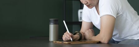 asian woman writing on tablet on table at home.work from home while coronavirus outbreak.leave space for add text.banner mockupの写真素材