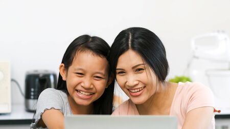 Mother and preteen daughter video call to grandparent in kitchen at home.family happy time.video conference with laptop.quarantine activity when outbreak of coronavirus.e-learning conceptの写真素材