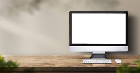 desktop computer on wood table backgorund with sunlight window create leaf shadow on wall with blur indoor green plant foreground.panoramic banner mockup for display of product,warm tone lightsの写真素材
