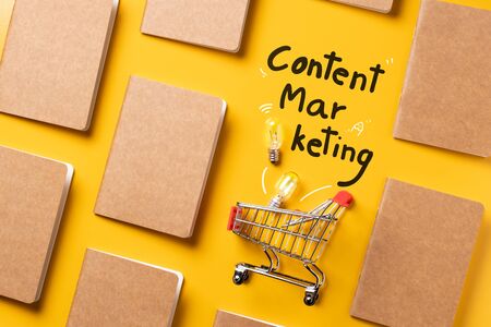 creativity content marketing concept,top view shopping cart with full of lightbulbs with Kraft paper book alignment in pattern on yellow desk surface.leave space for display your content.の写真素材