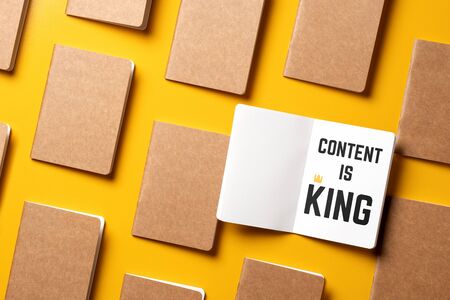 content is king for online marketing concept.top view of open notebook with golden crown align with kraft paper book in pattern on yellow table backgroundの写真素材