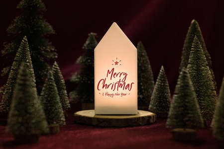 Merry christmas and happy new year text on home lamp with xmas tree on red velvet fabric table in dark night moodの写真素材