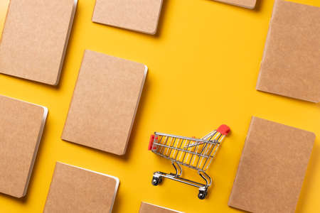 content marketing concept,top view Black and Kraft paper book alignment in pattern with shopping cart on yellow desk surface.leave space for display your contentの写真素材